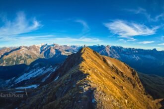 Solo trekker on a remote Himalayan high-altitude trail surrounded by dramatic snow-capped mountain peaks and open sky