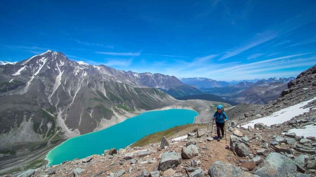 A trekker crosses a high-altitude mountain pass above the turquoise Ala-Kul Lake in Kyrgyzstan — a secret adventure travel destination