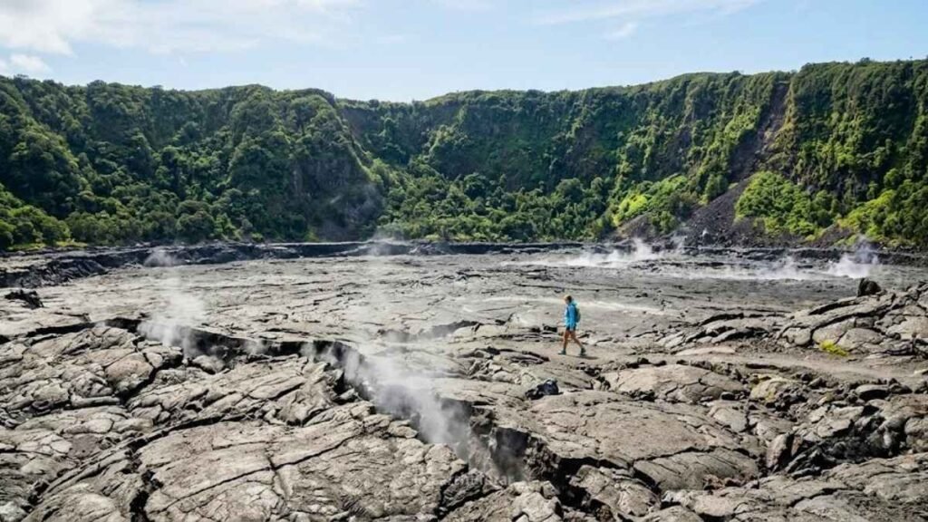 Hiker crossing the vast grey hardened lava lake of Kīlauea Iki crater inside Hawai'i Volcanoes National Park