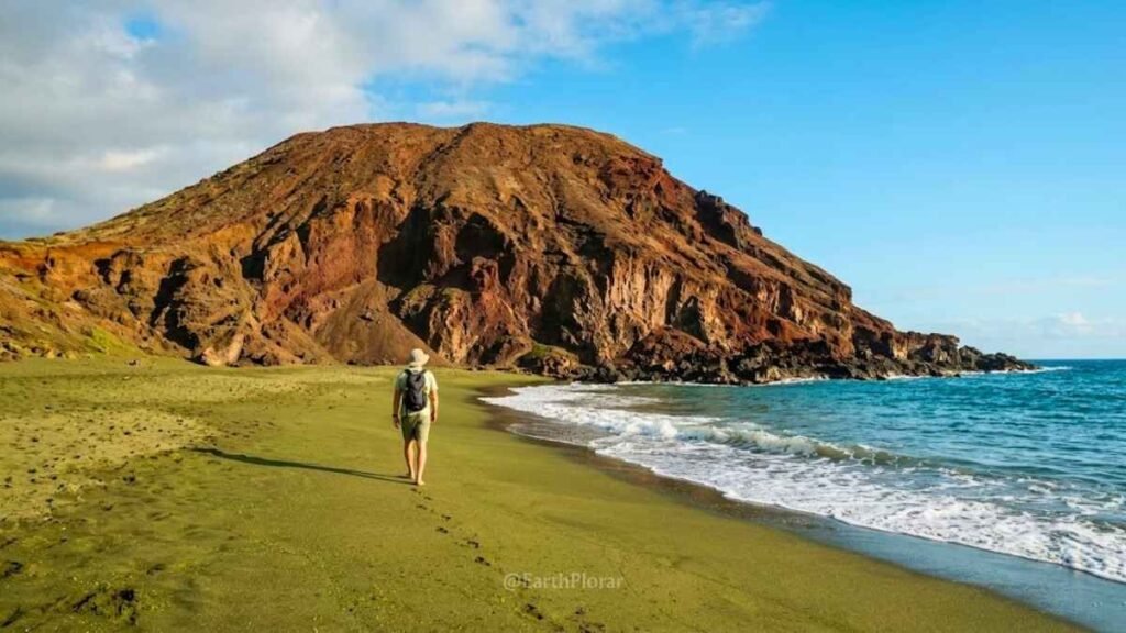 Traveler walking along Papakōlea's striking olive-green sand beach framed by a volcanic cinder cone on the Big Island
