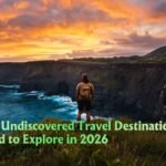 A lone traveller stands on a misty cliff edge overlooking one of the best Undiscovered Travel Destinations at golden hour