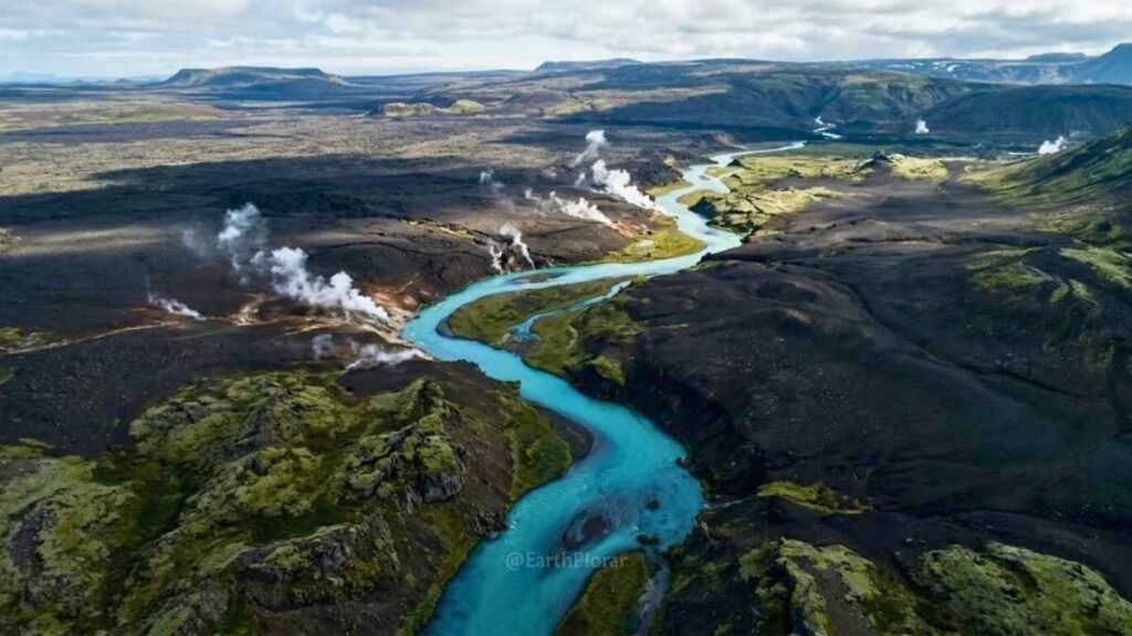 Aerial view of Iceland's volcanic landscape with lava fields, steam vents, and a turquoise river winding through black rock