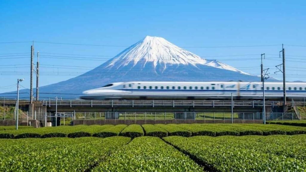 A Shinkansen N700 bullet train streaking past Mount Fuji on a clear day, sustainable travel Japan by rail