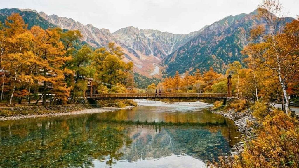 Kappa-bashi bridge over the Azusa River in Kamikochi alpine valley with autumn foliage and Japan Alps peaks