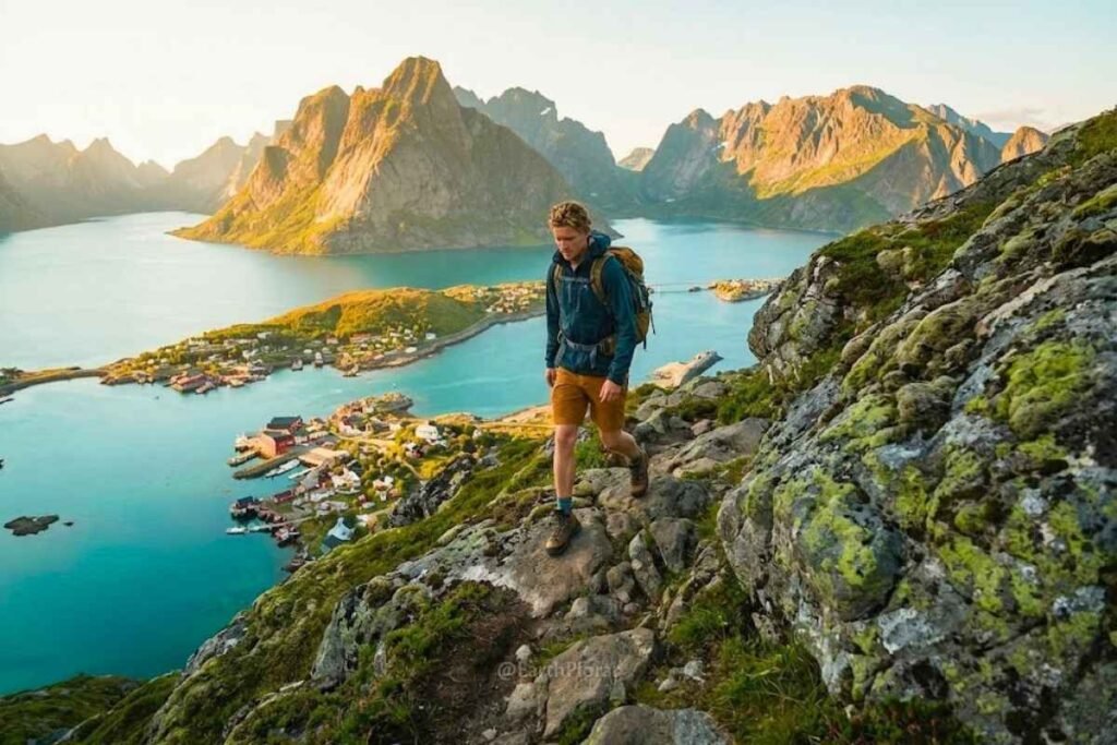 Hiker on a ridge trail overlooking Lofoten Islands fishing village, Norway